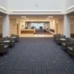modern lobby with grey armchairs, white walls, and blue patterned carpet tiles arranged in a grid.